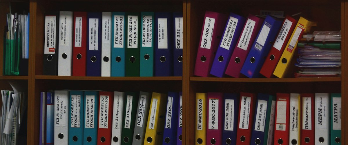 Rows of colorful ring binders organized on wooden shelves in an office