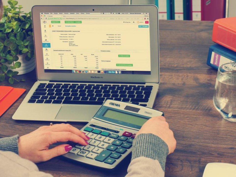 Working through billing figures at a calculator beside a laptop spreadsheet